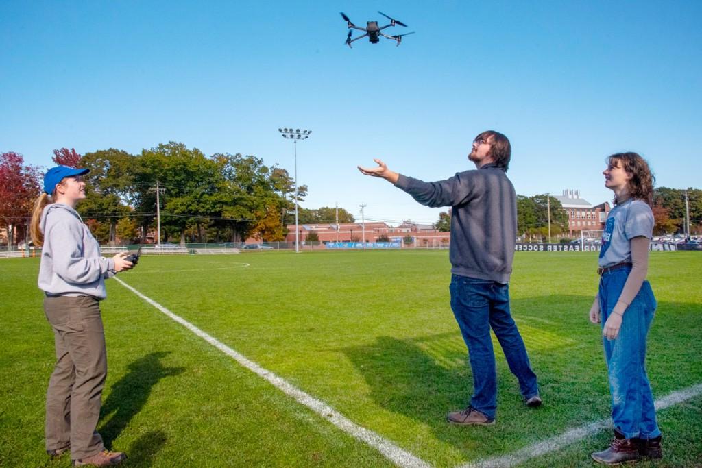 Three students flying a drone from a soccer field